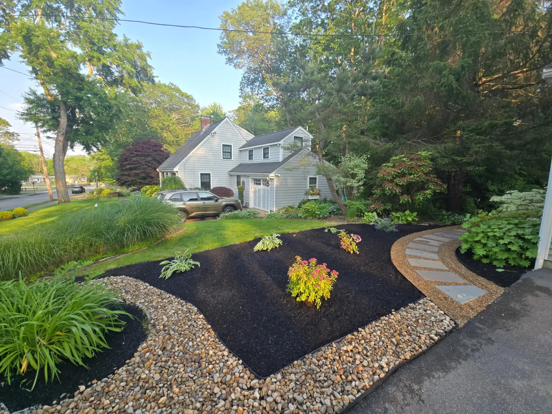 White house beside curved black mulch beds, green plants, stone edging, and a stepping-stone path
